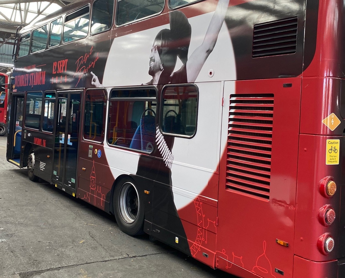 Nearside of the wrapped bus, doors visible, Aura World Tour creative across both decks
