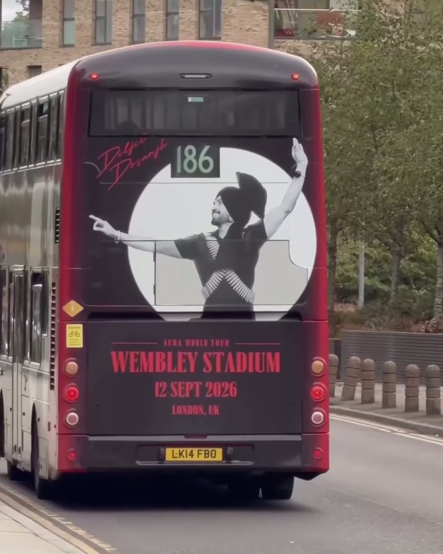 Rear of the Aura World Tour wrapped bus driving away along a north-west London road