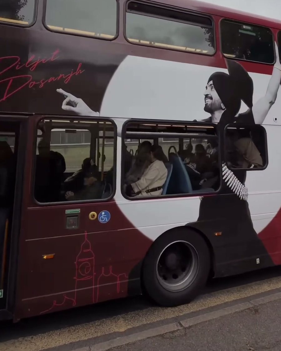 The wrapped bus passing on the nearside with its doors open, red skyline line along the lower deck
