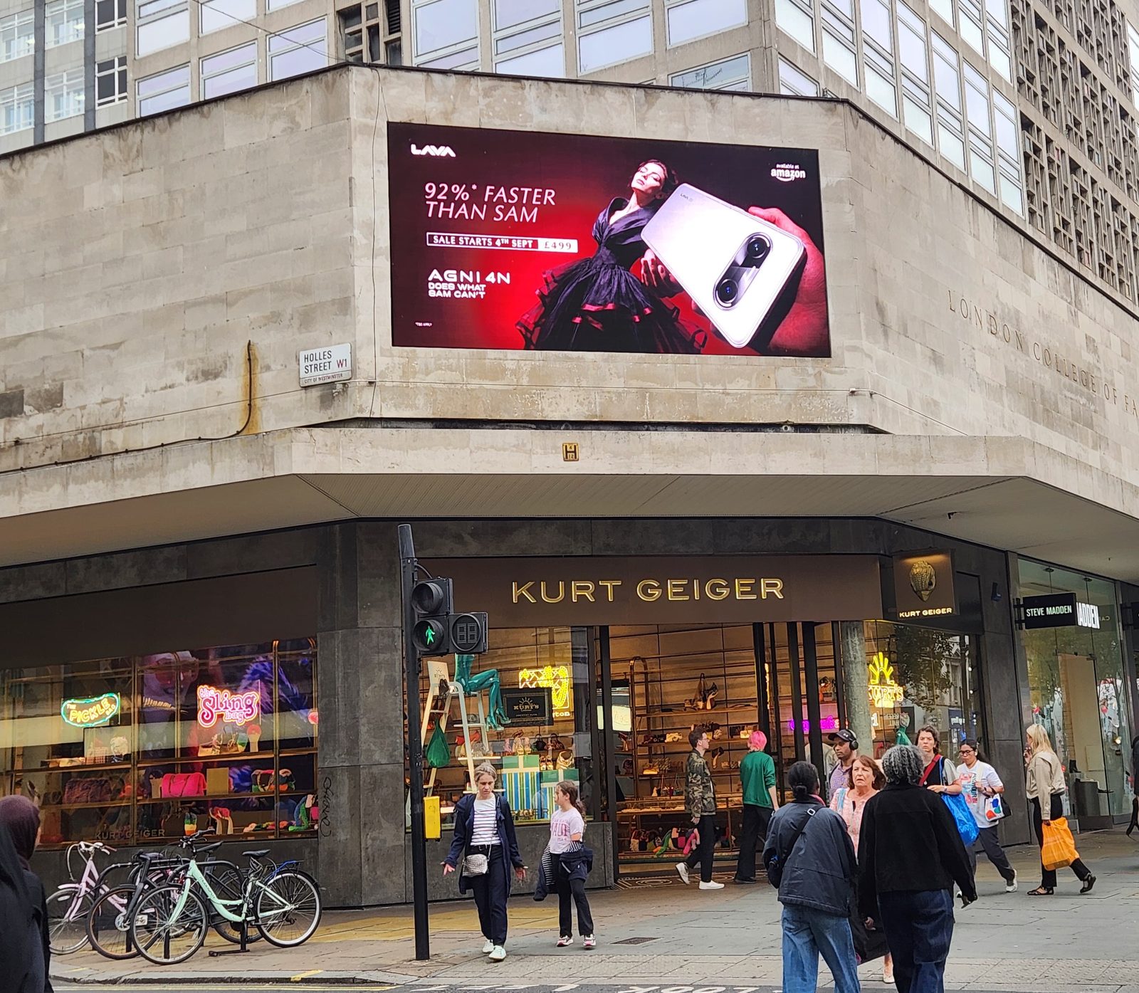The LAVA AGNI 4N advert on the landmark digital screen above Oxford Street at Holles Street, London, with shoppers crossing below