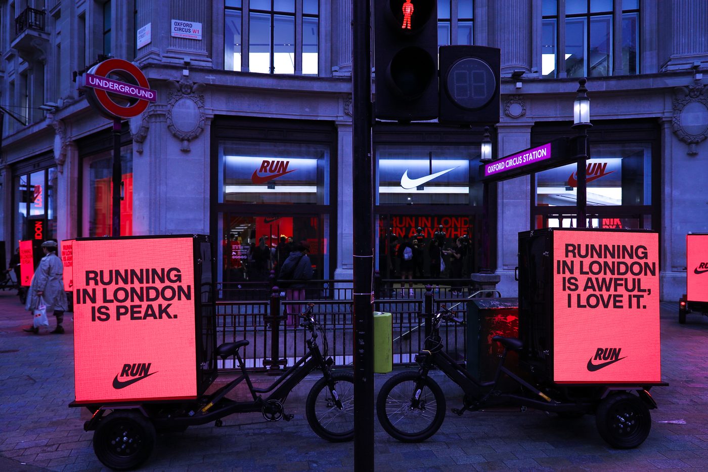 Two Nike Digital AdBikes parked outside the Nike store at Oxford Circus station at night with illuminated LED screens