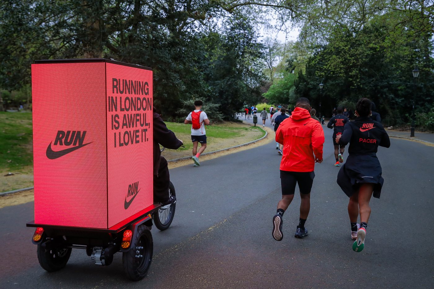 Nike Digital AdBike riding through a park path alongside marathon runners, showing motivational messaging on the LED screen