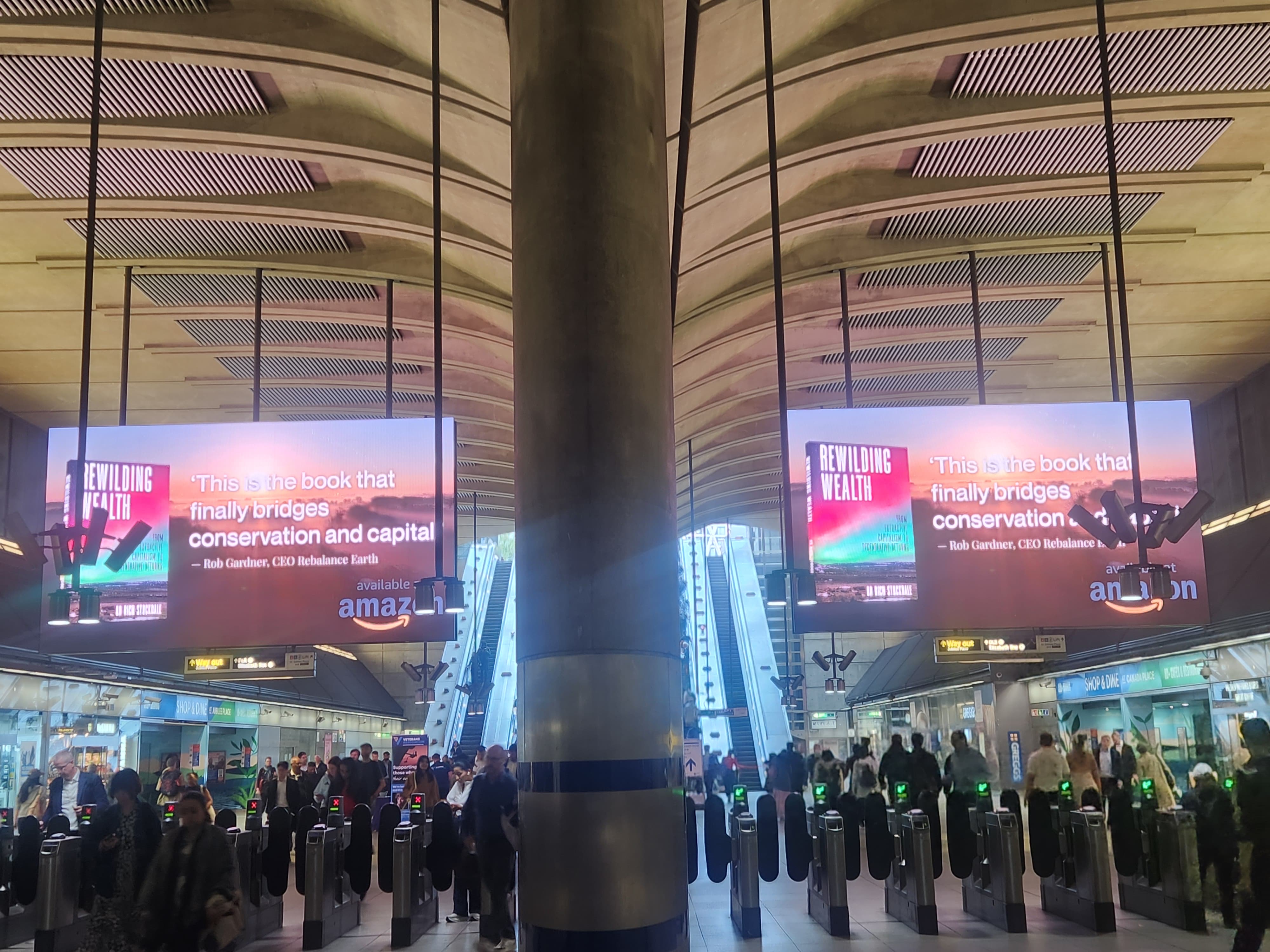Canary Wharf ticket hall during the evening commute with the Rewilding Wealth book launch campaign live on the Digital Gateway