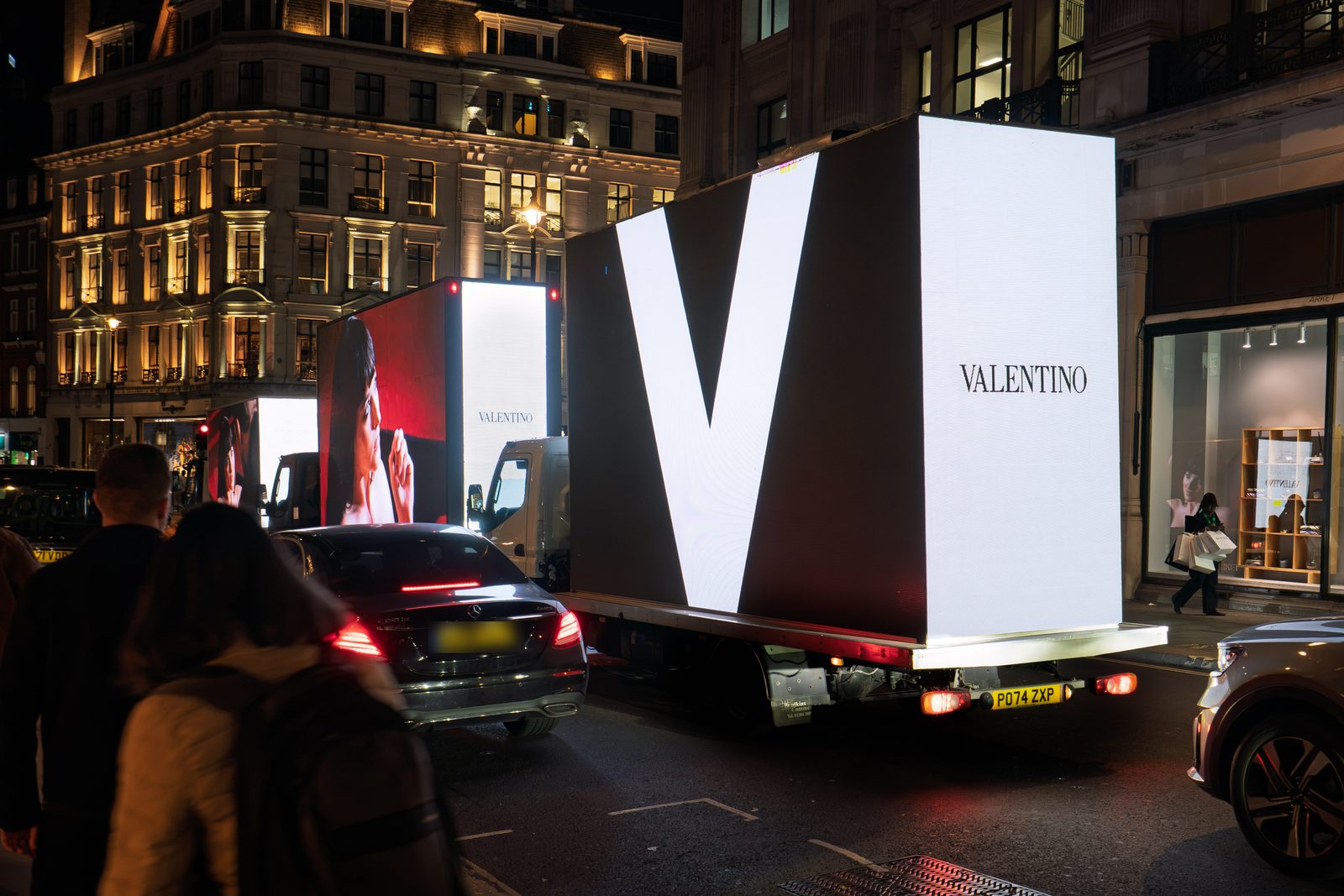 The giant white V and the VALENTINO wordmark on the back of a Monster AdVan on Regent Street at night, with the convoy ahead