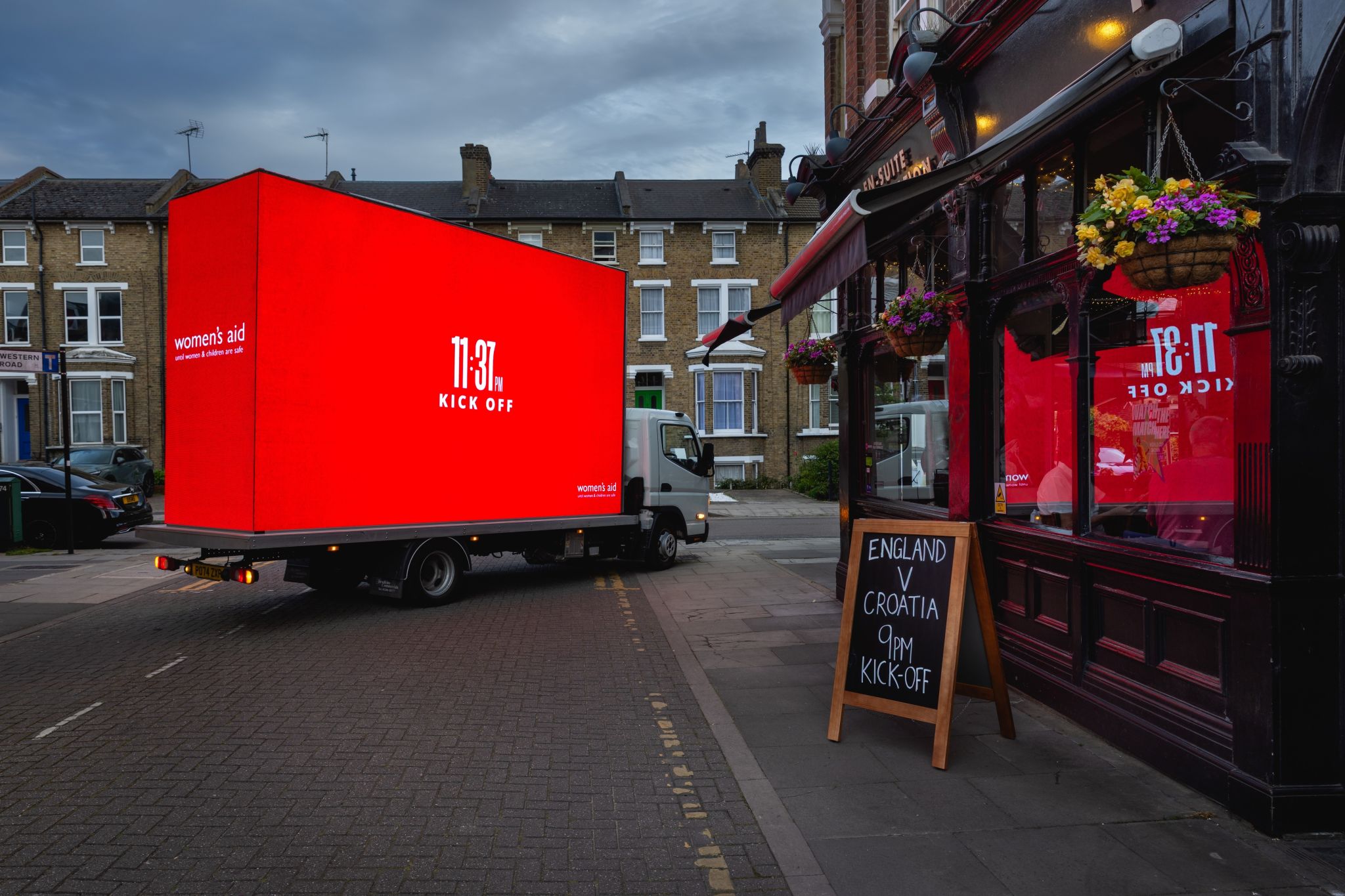 Monster Outdoor AdVan parked outside a London pub showing the red 11:37pm Kick Off Women's Aid creative, beside the pub's England v Croatia 9pm kick-off chalkboard